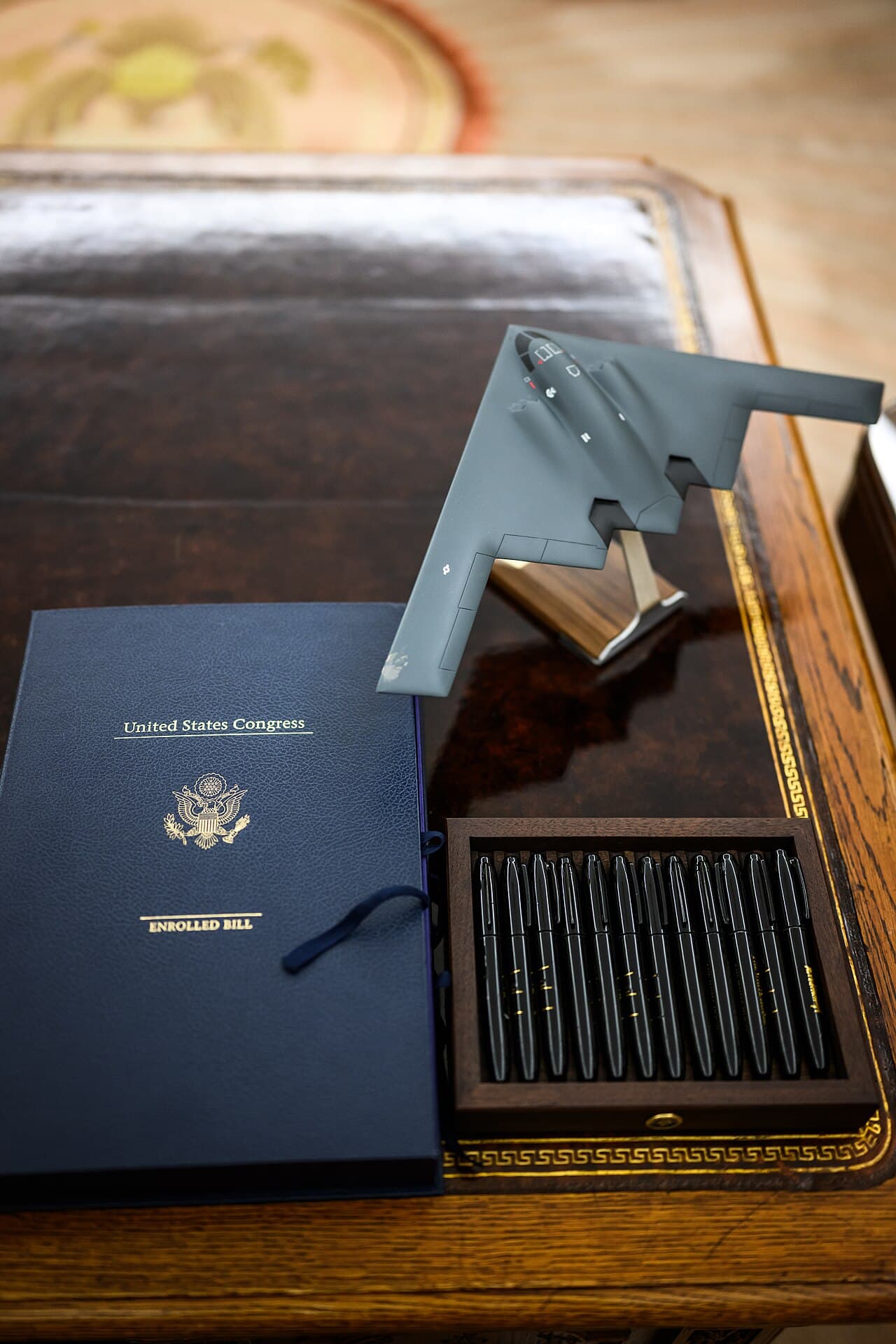 An enrolled bill from the United States Congress lying in its folder on the Resolute Desk in the Oval Office, beside a box of signing pens
