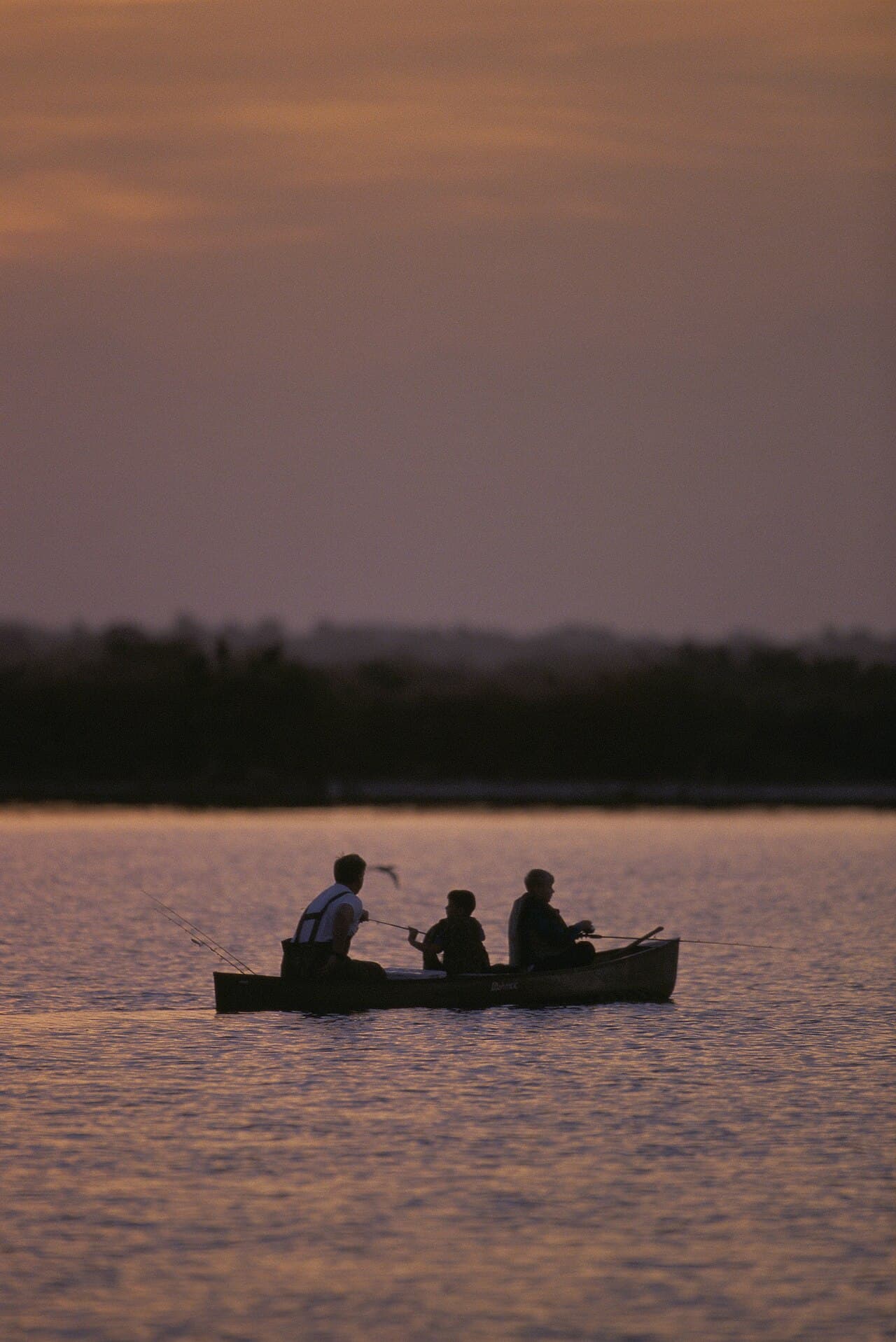 Anglers silhouetted in a small boat on open water at sunset
